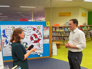 Gareth Davies MP with library staff in front of the summer reading challenge leader board